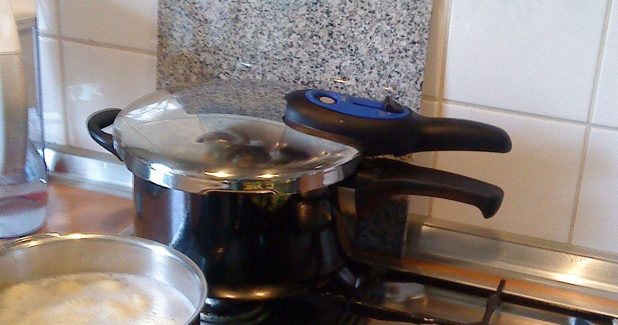 Offener Schnellkochtopf mit dampfenden goldgelben Kartoffeln auf moderner Küchenarbeitsplatte in warmem Licht