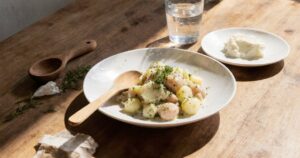 Draufsicht auf einen frisch angerichteten Kartoffelsalat in einer Schale mit Holzlöffel und Petersilie auf Holztisch.
