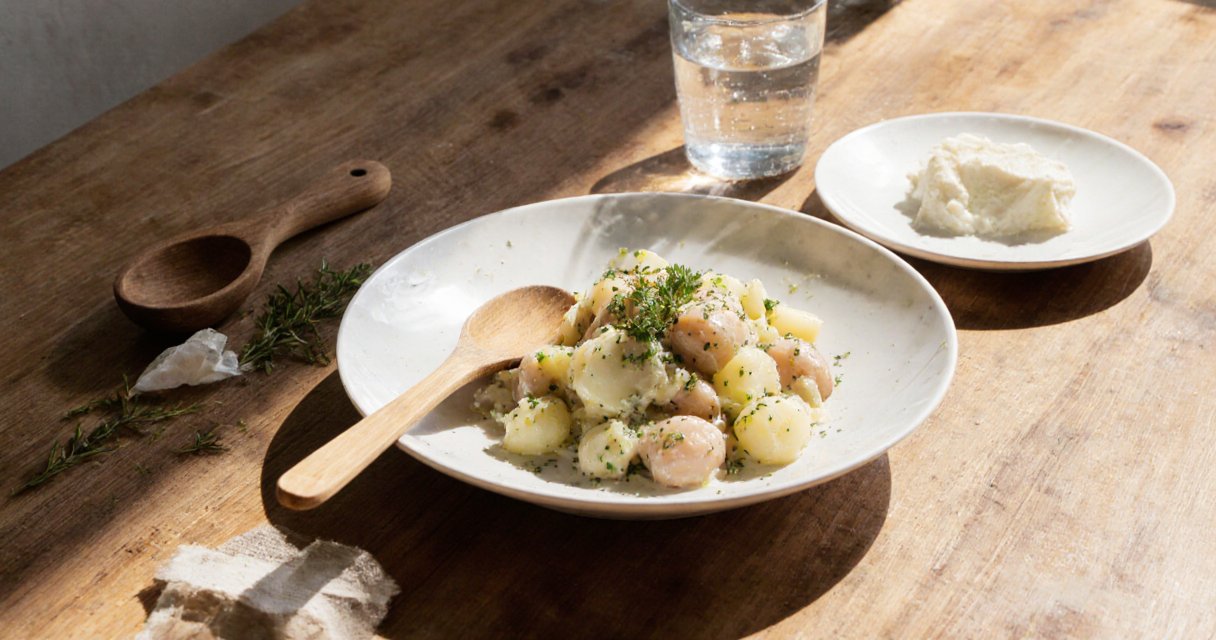 Draufsicht auf einen frisch angerichteten Kartoffelsalat in einer Schale mit Holzlöffel und Petersilie auf Holztisch.